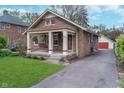 Brick home with a welcoming front porch, hanging plants, and a driveway leading to a detached garage at 914 Kessler Blvd E Dr, Indianapolis, IN 46220
