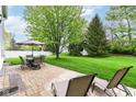 A beautiful backyard with a stone patio, an outdoor dining set, lounge chairs, and a large shade tree at 10524 Hawks Ridge Ct, Fishers, IN 46037