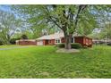 A brick home with green lawn is shaded by a large tree in a well-landscaped suburban setting at 4044 Roamin Dr, Greenwood, IN 46142