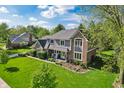 An aerial view of a charming house on a lush green lawn with mature trees around it, under a blue sky at 1508 Redwood Dr, Carmel, IN 46032