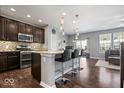 Open kitchen with granite island, pendant lights, stainless steel appliances, and hardwood floors, leading to living area at 9422 Oakley Dr, Indianapolis, IN 46260