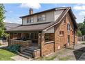 A brick two-story home featuring a covered front porch, mature trees, and a well-maintained lawn at 6051 Lowell Ave, Indianapolis, IN 46219