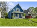 View of a charming blue house with a covered front porch, set against a backdrop of green lawn and trees at 1130 W Congress Ave, Indianapolis, IN 46208