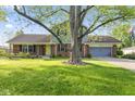 A charming brick and siding two-story home with an attached garage has a well-kept lawn and a large tree at 7153 N Audubon Rd, Indianapolis, IN 46250