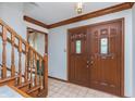 Inviting entryway with double doors featuring glass inserts, wood trim, tiled floor, and wooden staircase at 1421 Stoney Creek Cir, Carmel, IN 46032