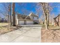 Rear view of house featuring three-car garage and long drive in a wooded setting at 3948 S Woodfield Dr, New Palestine, IN 46163