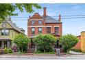 A stately brick home with mature trees, showcasing classic architecture under a clear sky at 419 N College Ave, Indianapolis, IN 46202