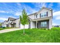 Inviting two-story home with a manicured lawn and young tree, gray siding, black brick, and an attached two-car garage at 10236 Arctic Edge Dr, Indianapolis, IN 46239