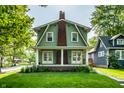 View of home featuring green clapboard siding, brick chimney, covered front porch, and manicured lawn at 357 N Kenyon St, Indianapolis, IN 46219