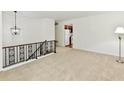 Neutral loft area with carpet, decorative railing, and view into the kitchen at 5225 Elderberry Rd, Noblesville, IN 46062
