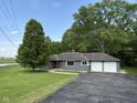 Ranch-style home with a two-car garage, mature tree and an asphalt driveway surrounded by a well-manicured lawn at 7897 Moore Rd, Indianapolis, IN 46278