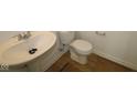 Compact bathroom featuring a pedestal sink, efficient toilet, and wood-look flooring, offering functionality in a small space at 10126 Redwood Peak Ln, Indianapolis, IN 46259