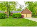 Charming brick home featuring a two-car garage and a lush green lawn surrounded by mature trees at 9324 W Point Pl, Indianapolis, IN 46268