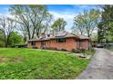 Inviting red brick house with solar panels, a driveway, and mature trees creating a serene and private setting at 3975 Denwood Dr, Indianapolis, IN 46226
