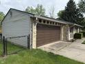 Side view of the stone home featuring an attached garage and fenced yard at 802 Suwanee Ct, Indianapolis, IN 46217