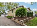 Quaint home featuring a lush green yard, unique block retaining wall, and attached garage at 944 N Harbison Ave, Indianapolis, IN 46219