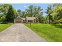 Wide view of a single-story home with an attached garage and a long driveway, surrounded by lush green landscaping at 5015 E 70Th E St, Indianapolis, IN 46220