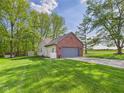 View of a home with a two-car garage, beautiful lawn, and verdant trees at 1356 S Catamaran Cir, Cicero, IN 46034