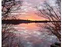 A serene sunset reflected on the lake, framed by silhouetted tree branches in the foreground at 7400 Oakbay Dr, Noblesville, IN 46062