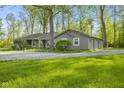 Cozy home with a gravel driveway, wooden porch, and garage surrounded by mature trees at 5039 Five Points Rd, Indianapolis, IN 46239