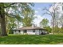 A wide-angle shot of a single-story brick home with a lush lawn and mature trees on a sunny day at 13765 Howe Rd, Fishers, IN 46038