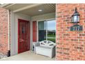 Inviting front porch featuring brick facade, red storm door, and bench at 217 Devonshire Ct, Anderson, IN 46013