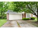Charming brick home featuring a two-car garage, mature landscaping, and healthy shade tree at 7703 Park North Lake Dr, Indianapolis, IN 46260