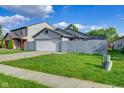 Exterior view of home with a white garage door, gray fence, lush grass, and concrete driveway at 6707 Greendale Ln, Indianapolis, IN 46241