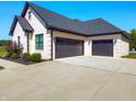 Attached three-car garage with black doors and concrete driveway, surrounded by lush landscaping and brick exterior at 8112 Joni Ave, Martinsville, IN 46151