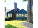 Quaint home with brick chimney, white-trimmed windows, and a lush green lawn accentuated by a large tree at 310 S Butler Ave, Indianapolis, IN 46219