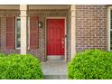 Close-up of a vibrant red front door framed by brickwork and lush green bushes at 7023 Hartington Pl, Indianapolis, IN 46259