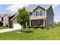 Two-story home featuring green siding, brick accents, an attached two car garage and a well-manicured front yard at 928 Cherry Tree Ln, Greenwood, IN 46143