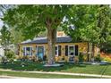 Charming yellow home featuring a well-manicured lawn, mature tree, and colorful floral arrangements at 3433 Brewer Dr, Indianapolis, IN 46222