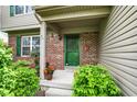 A cozy front porch with brick accents, green door, potted flowers, and trimmed bushes at 5523 Gainesway Dr, Greenwood, IN 46142