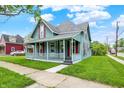 View of a quaint two-story home showcasing a covered porch, red shutters, and lush green yard at 538 N East St, Greenfield, IN 46140