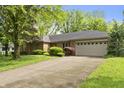 Inviting brick home featuring an attached two-car garage, a well-maintained lawn, and mature trees at 8909 Ellington Dr, Indianapolis, IN 46234
