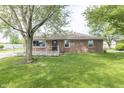 A lush green backyard with a rustic brick home, a wooden deck, and mature trees at 156 N Eastern Village Dr, Greenfield, IN 46140