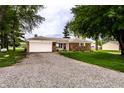 Ranch-style brick home with an attached garage and gravel driveway surrounded by mature trees at 2965 E 1100 N, Pendleton, IN 46064