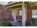 Front entrance with brick siding, wooden door, wind chimes, and manicured landscaping at 7587 Winding Way, Fishers, IN 46038