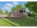 A charming brick home with a cozy front porch, a retaining wall, and a well-manicured lawn at 6102 Primrose Ave, Indianapolis, IN 46220