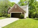 Side view of brick house with two car garage, paved driveway, and manicured shrubs at 6242 Carrington Dr, Indianapolis, IN 46236