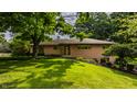 Well-maintained one-story home with brick facade, mature trees, and green lawn at 7887 Meadowbrook Dr, Indianapolis, IN 46240