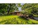 Well-maintained one-story home with brick facade, mature trees, and green lawn at 7887 Meadowbrook Dr, Indianapolis, IN 46240