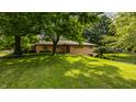 Well-maintained one-story home with brick facade, mature trees, and green lawn at 7887 Meadowbrook Dr, Indianapolis, IN 46240