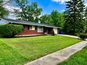 Low angle view of a red brick home with lush green lawn, mature trees, and concrete sidewalk at 3633 Tiffany Dr, Indianapolis, IN 46226