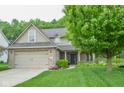 Lovely home featuring a lush green lawn, mature tree, brick accents, and a welcoming front entrance at 7322 Stones River Dr, Indianapolis, IN 46259