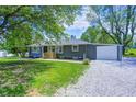 Charming single-story home with gray siding, a welcoming wooden porch, well-maintained lawn, gravel driveway, and attached garage at 5941 North St, Stilesville, IN 46180