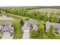Beautiful aerial view of a brick home with a pond, manicured lawn, and mature trees at 9598 N Mariners Crst, McCordsville, IN 46055