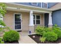 A welcoming front porch with brick pillars, lush landscaping, and a stylish door, creating a warm entry at 220 Sawdust Trl, Greenfield, IN 46140