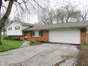 Home with attached garage and cracked driveway, showing brick and siding details, beneath budding trees at 2414 Constellation Dr, Indianapolis, IN 46229
